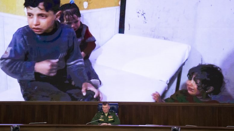 Russian Defense Ministry spokesman, Maj. Gen. Igor Konashenkov, speaks at a briefing in front of a screen showing Syrian children in a hospital at a briefing at the Russian Defense Ministry in Moscow on Friday, April 13. Konashenkov accused Britain of staging a fake chemical attack in the Syrian town of Douma last weekend. (AP Photo/Alexander Zemlianichenko)